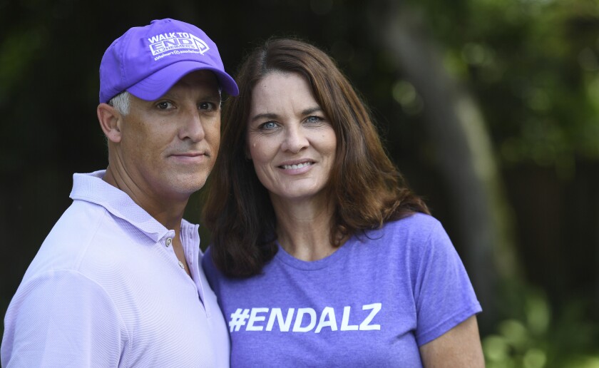 Michele and Doug Hall stand in their backyard. She wears a T-shirt that says #EndAlz.