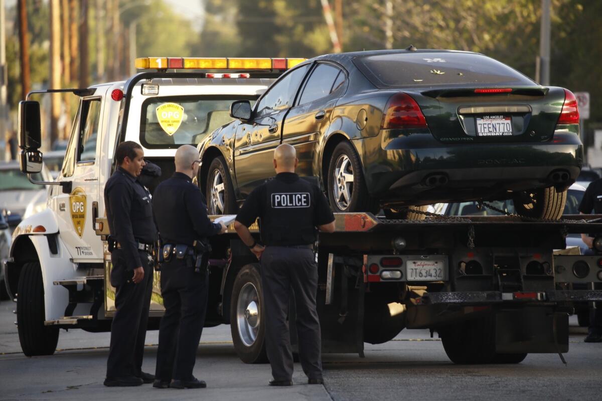 LAPD gang detectives watch as a bullet-riddled car is taken away after a woman was shot in the Hyde Park neighborhood of South L.A. early Wednesday morning.