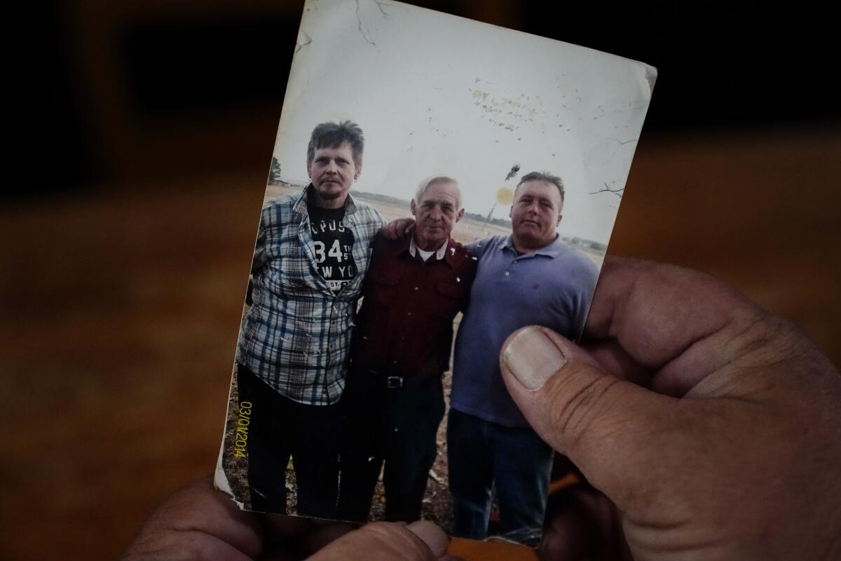 Daniel Guess holds a photograph of himself, right, along with his father, Larry Guess, center, and brother David Guess