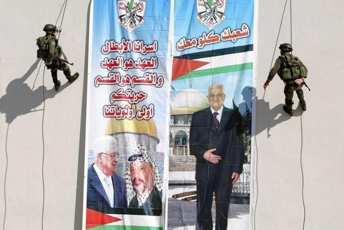 Palestinian security officers in Jenin, West Bank, make their way down a building adorned with a banner bearing images of Palestinian Authority leader Mahmoud Abbas, left, and his late predecessor, Yasser Arafat.