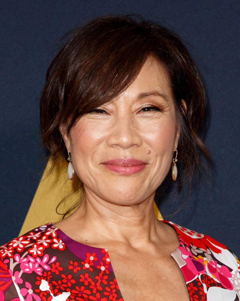 A beaming woman with dark brown hair wearing a floral-print shirt.