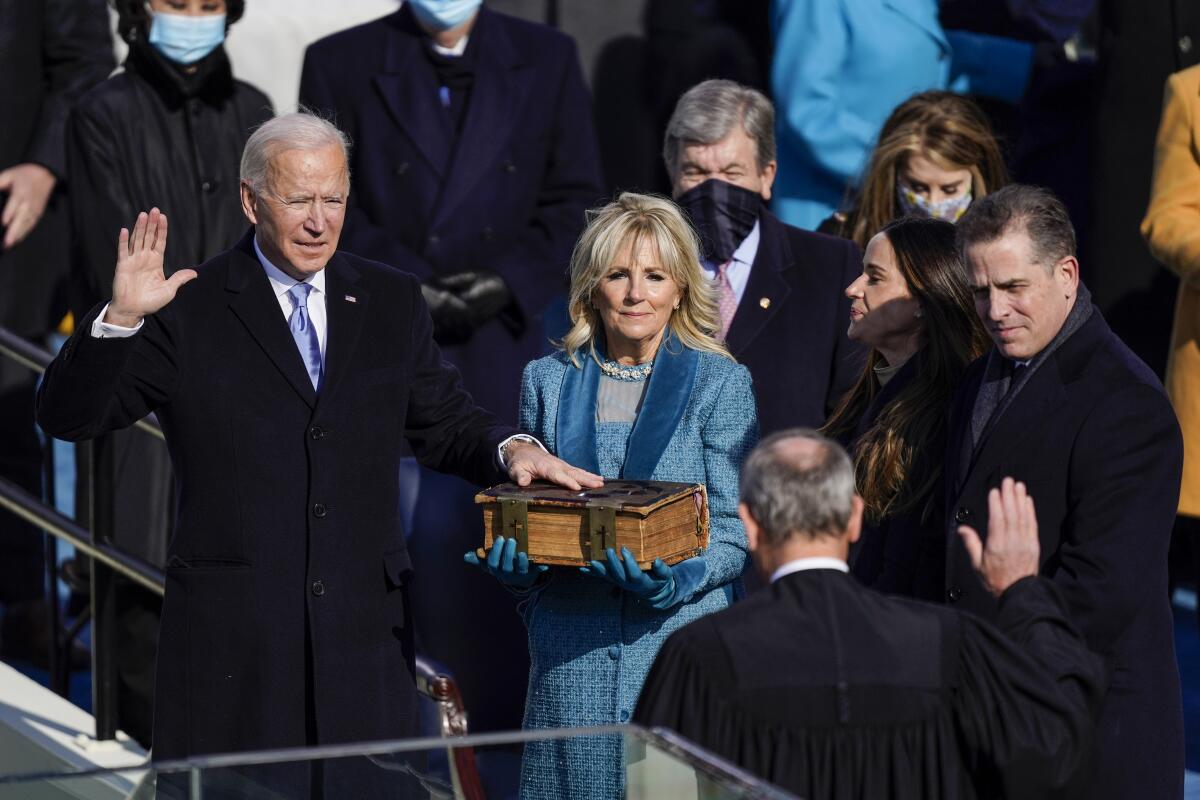 Joe Biden has a hand raised and his other on a Bible held by Jill Biden. Chief Justice John G. Roberts Jr. has a hand raised.