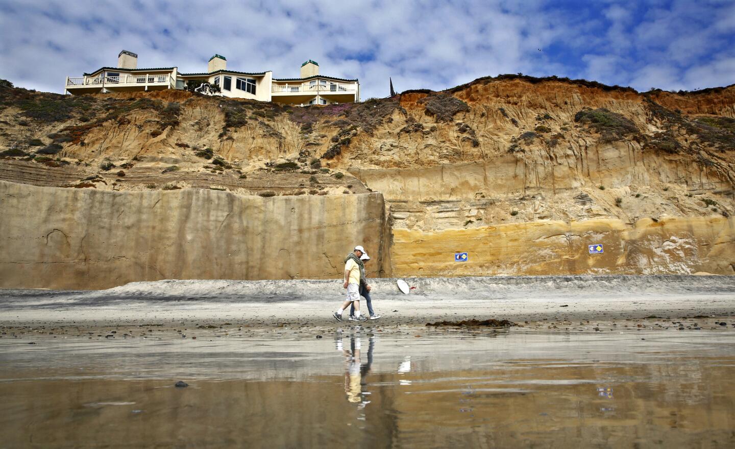 A couple walks on along the beach at low tide in Solana Beach, past a reinforced, 40-foot-high concrete sea wall below the condominiums on South Sierra Avenue. Homeowners say the sea walls are the only way to protect their properties. They are suing over a city decision on sea wall permits.