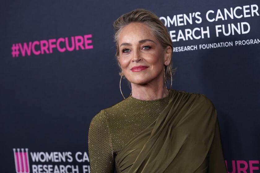 A woman with short blond hair smiles on the red carpet in a sparkling wrap gown