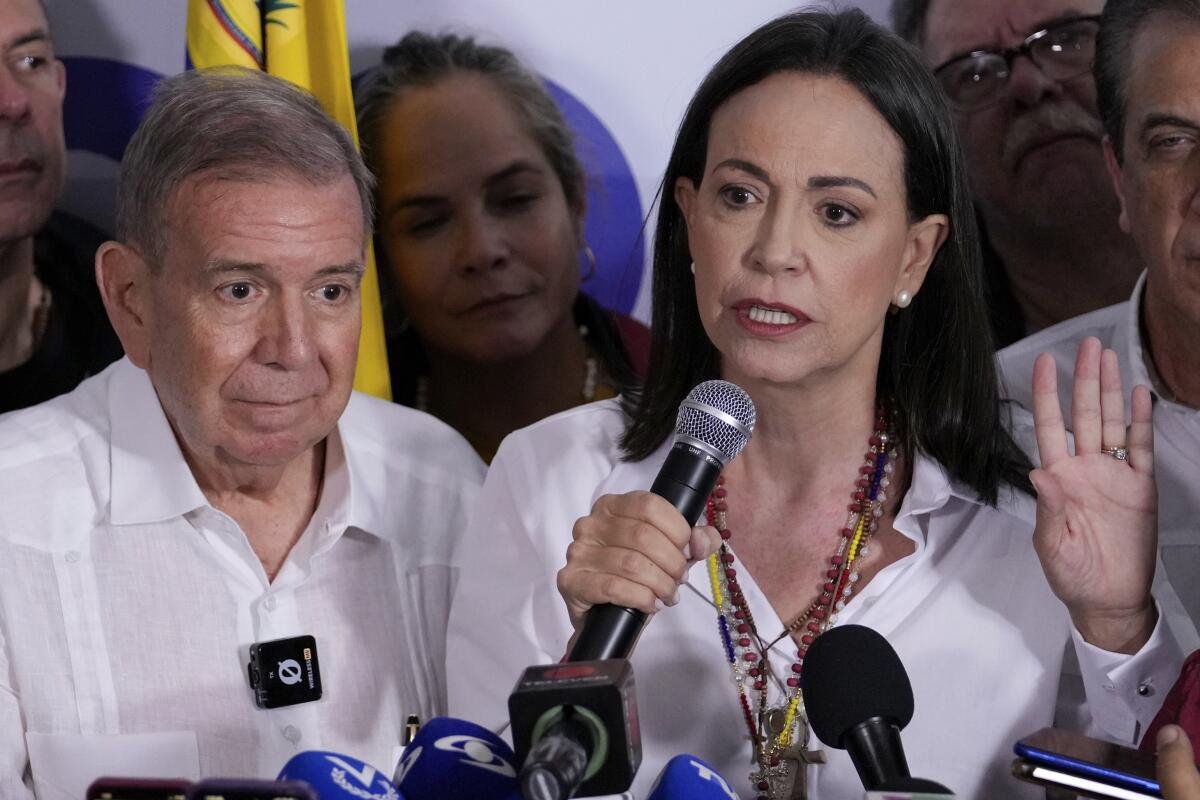 A woman speaks into a microphone as a man stands beside her.