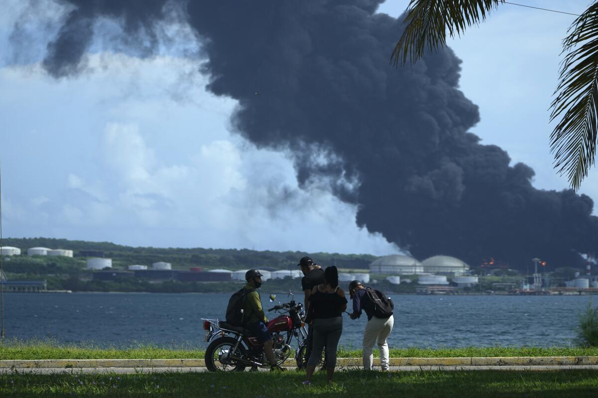 People watch as a huge plume of smoke rises over a body of water