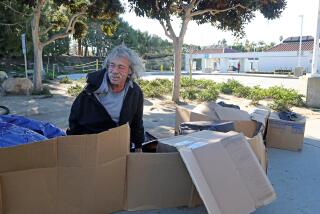 Gregory Scafferty, 62, sits in his cardboard bed in front of the Newport Transportation Center on Thursday morning in Newport Beach. A group of homeless people said they are being treated unfairly by both the city and the OCTA. (Kevin Chang / Daily Pilot)