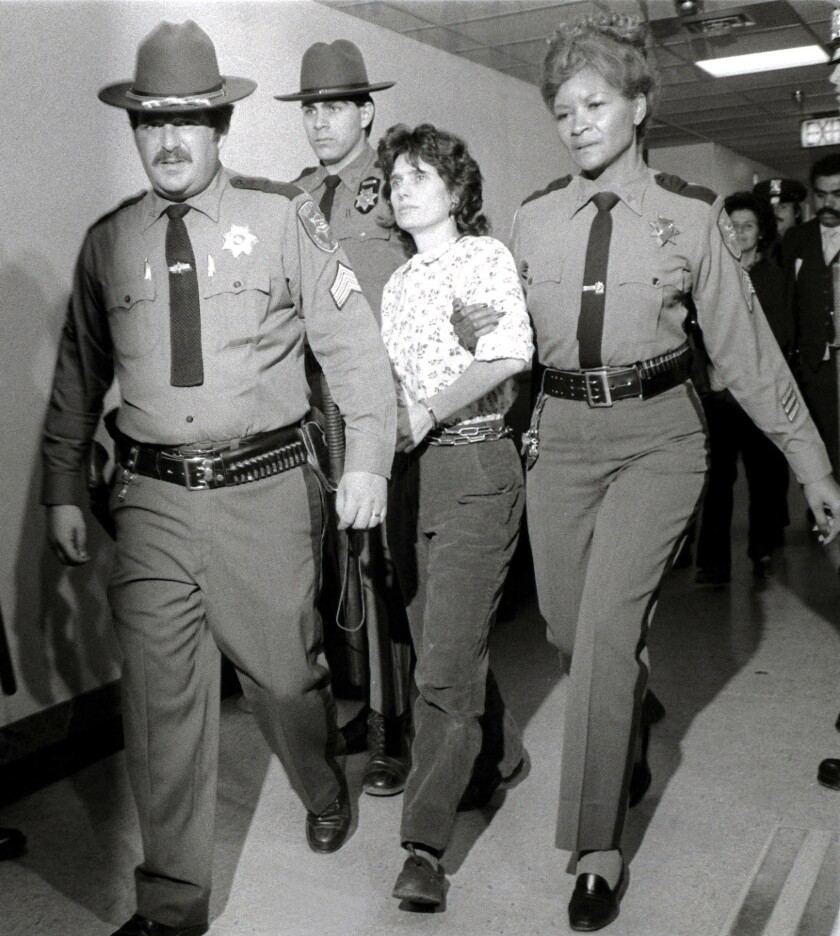 A black-and-white photo of sheriff's officers leading a young Kathy Boudin down a hall