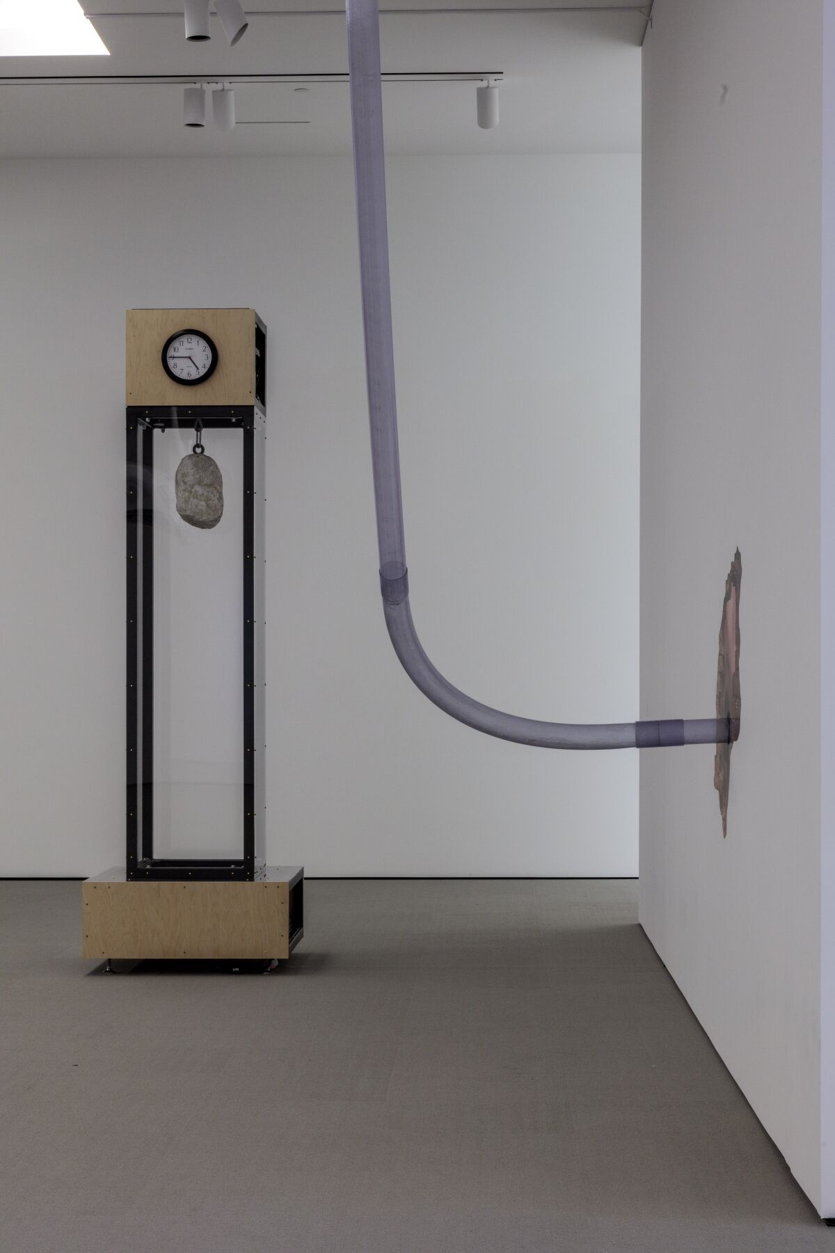A structure with a clock and hanging a rock, left, and a tube going into a wall