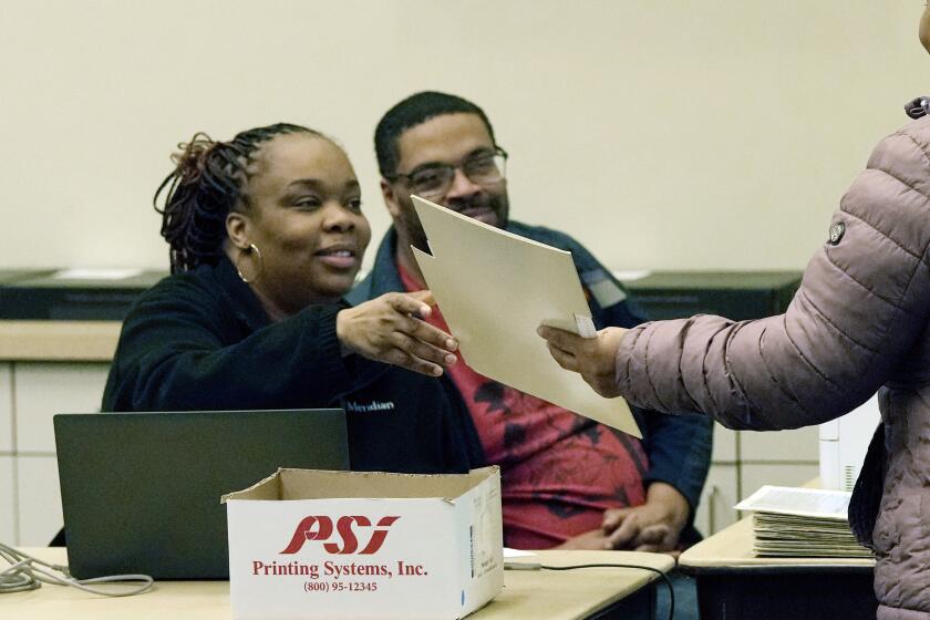 ARCHIVO - Una votante, a la derecha, recibe una papeleta durante la votación anticipada en el ayuntamiento de Warren, el 21 de febrero de 2024, en Warren, Michigan. (AP Foto/Carlos Osorio, Archivo)