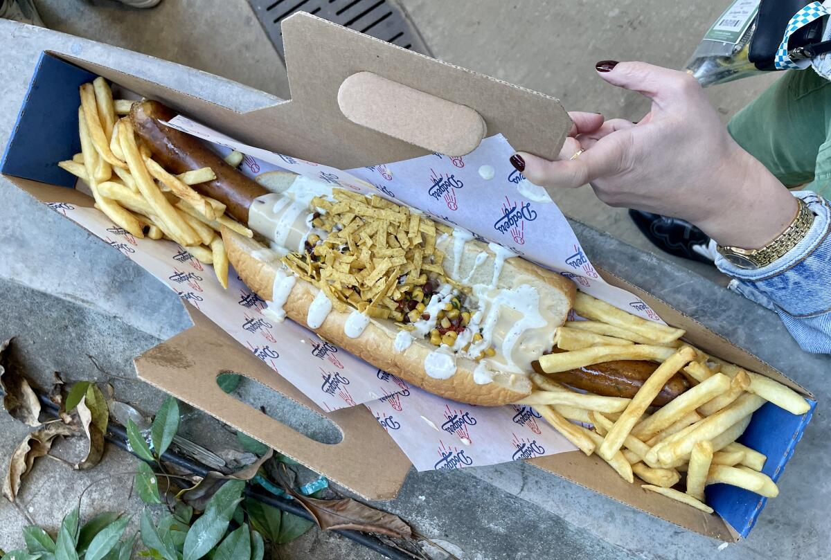 A to-go box holding a 16-inch sausage in a bun with dressing and French fries