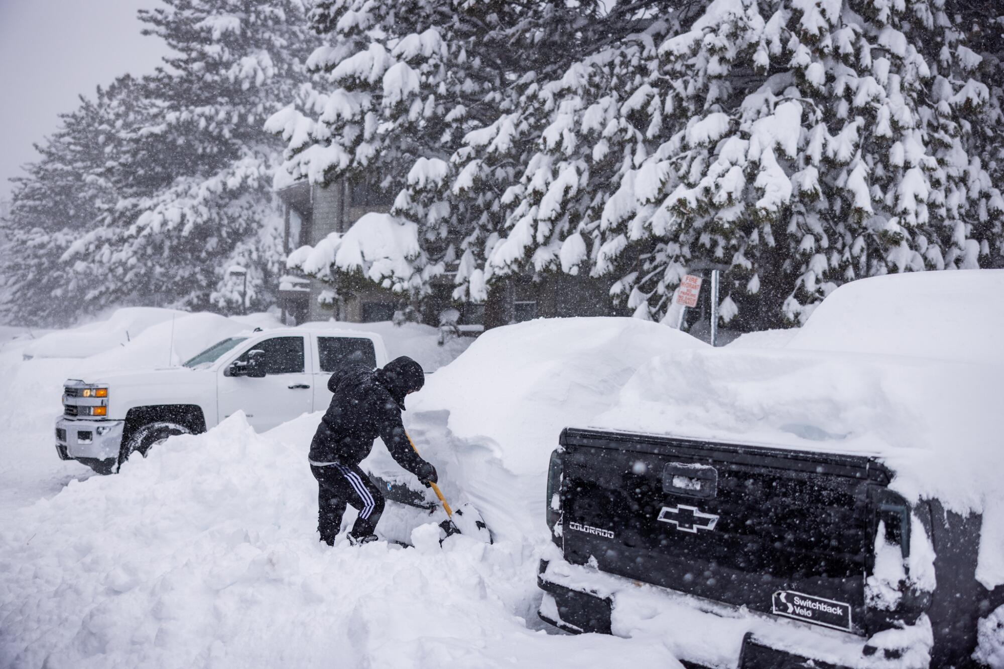 A person uses a shovel on a parked car that is completely covered in snow.