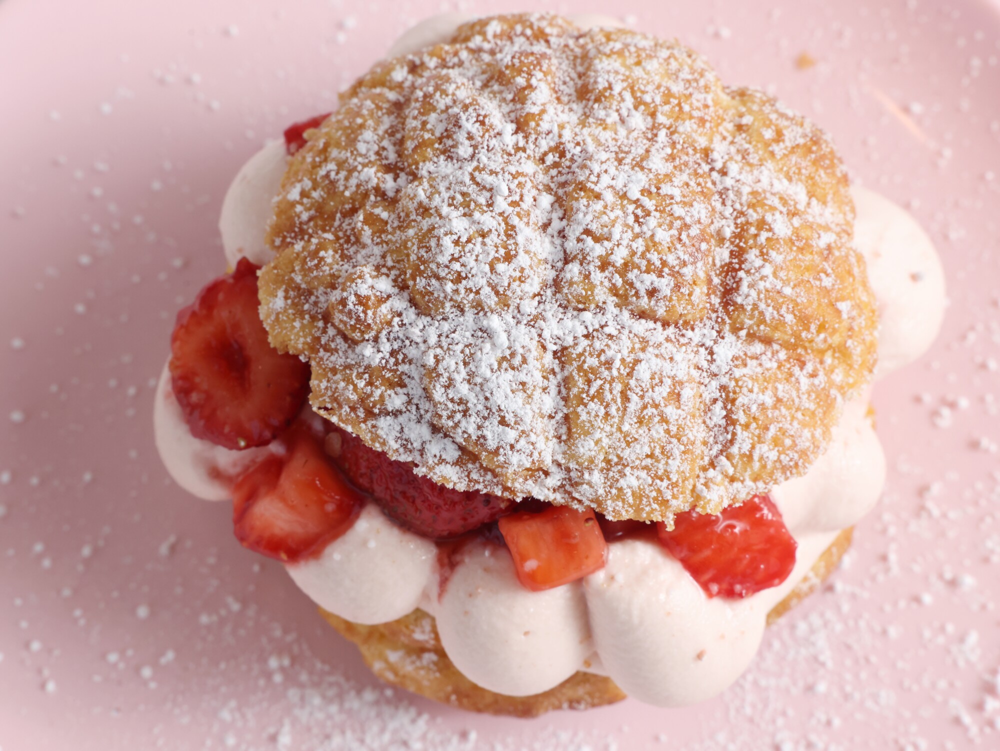 A strawberry shortcake bolo sits on a pink plate.
