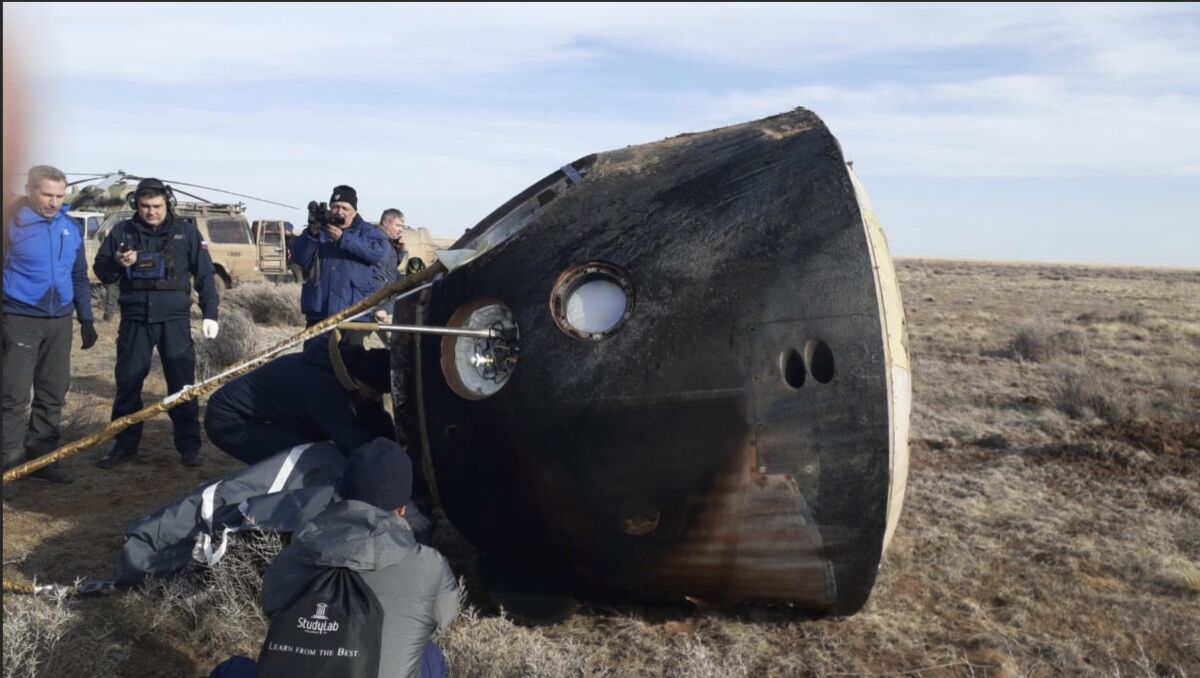 The Russian Soyuz MS-19 space capsule lies on the ground in a field.