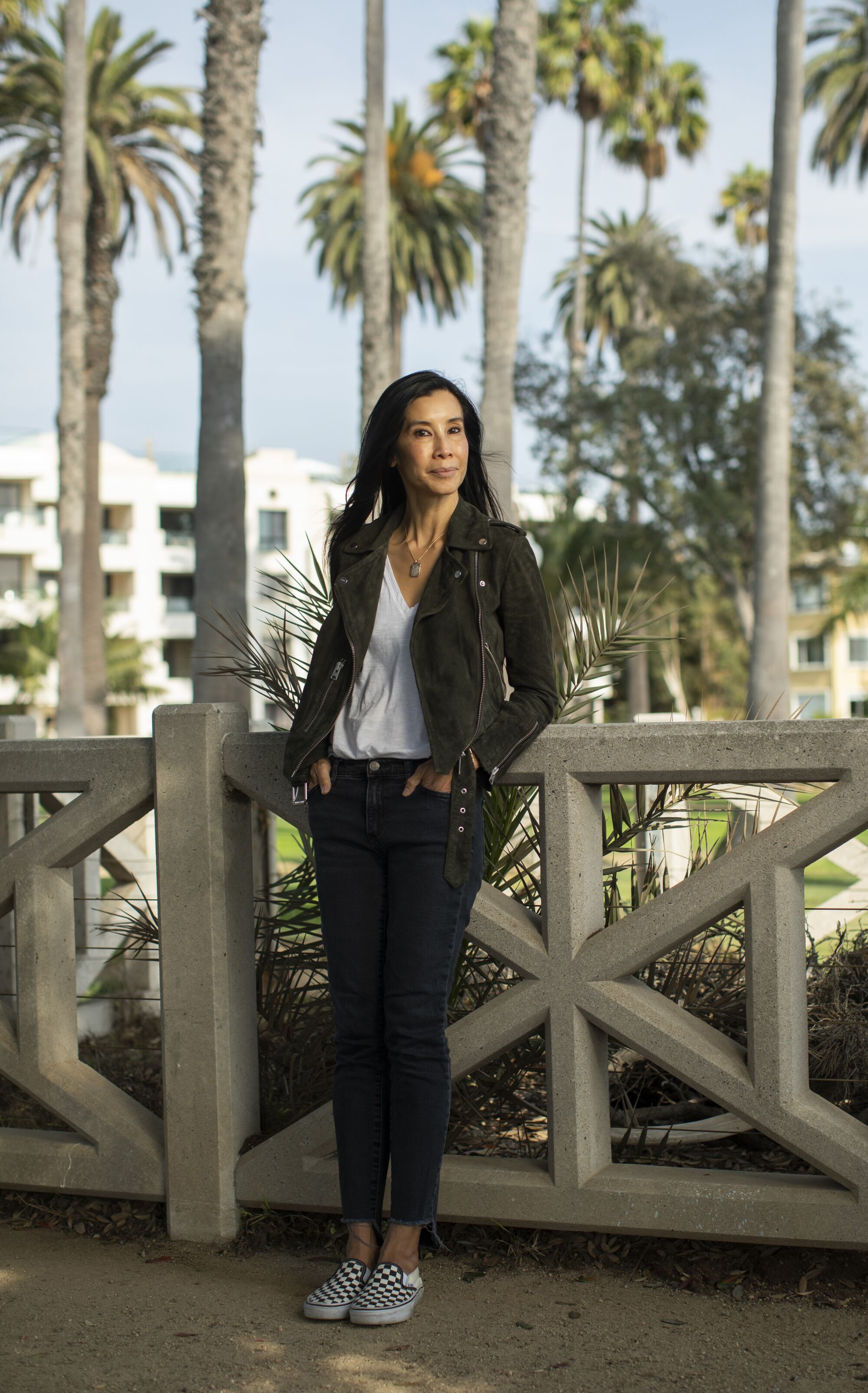 Lisa Ling leans against a decorative concrete railing, with palm trees in the background.