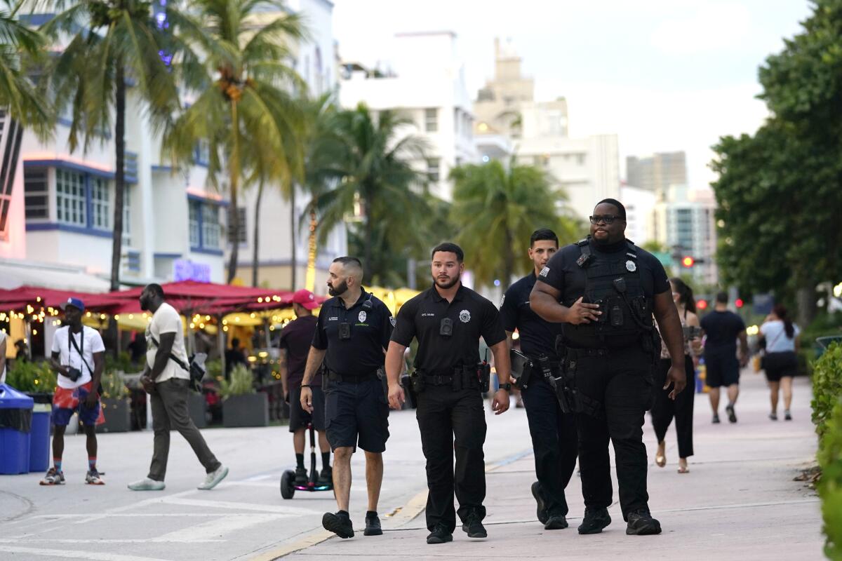 Code enforcement and police officers patrol along  a pedestrian walkway amid palm trees