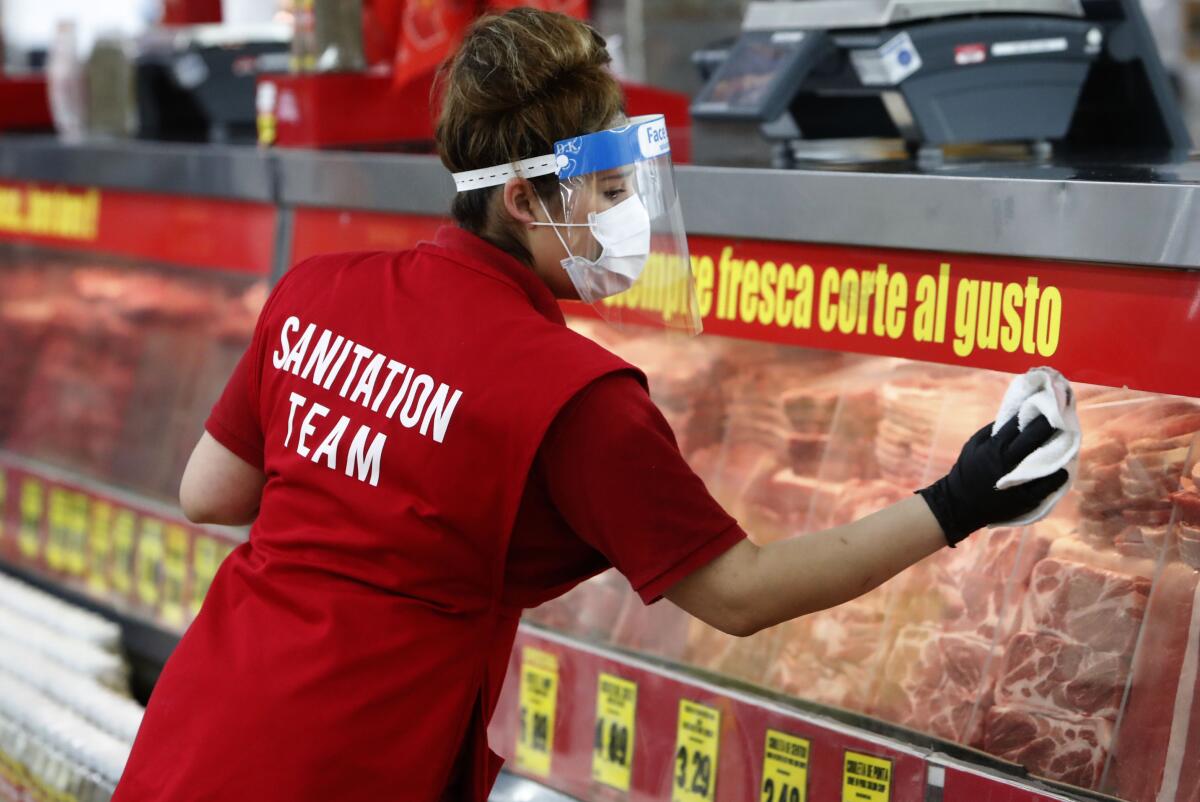 A woman wearing a face shield wipes down a display case