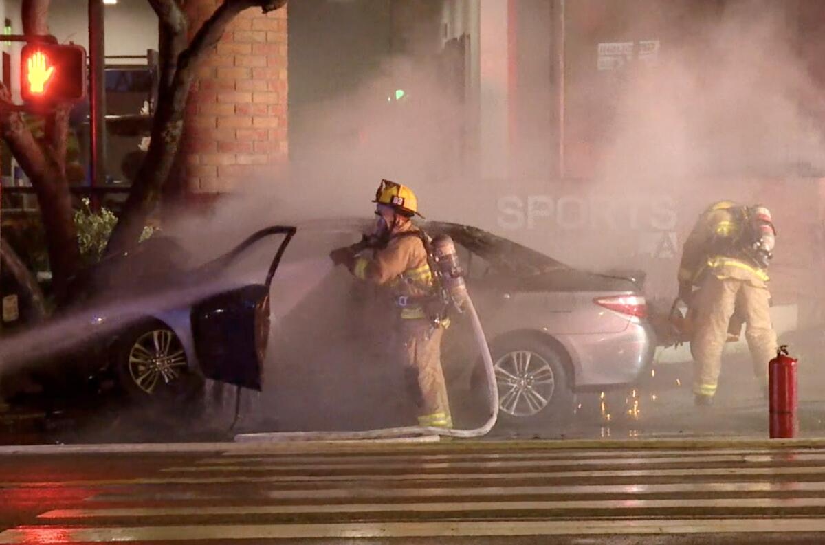 Firefighters spray down a car that had burned on a city street.