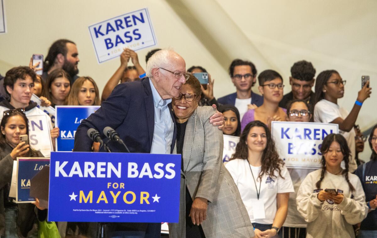  Sen. Bernie Sanders hugs Los Angeles mayoral candidate Karen Bass in front of several people with Karen Bass signs.
