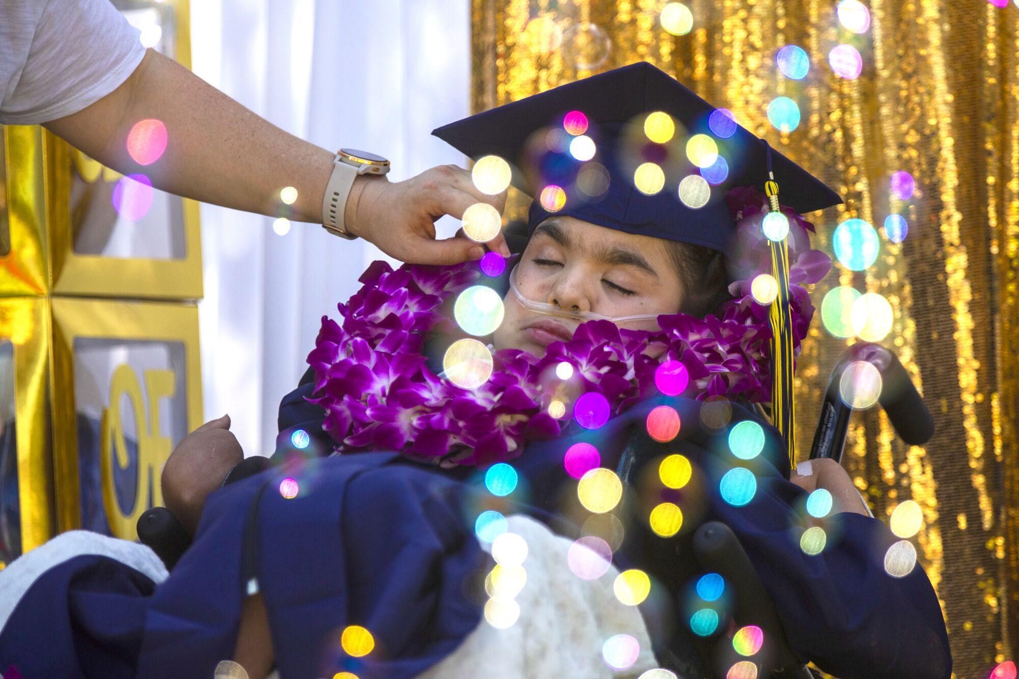 A young woman in a wheelchair wears a dark blue cap and gown.