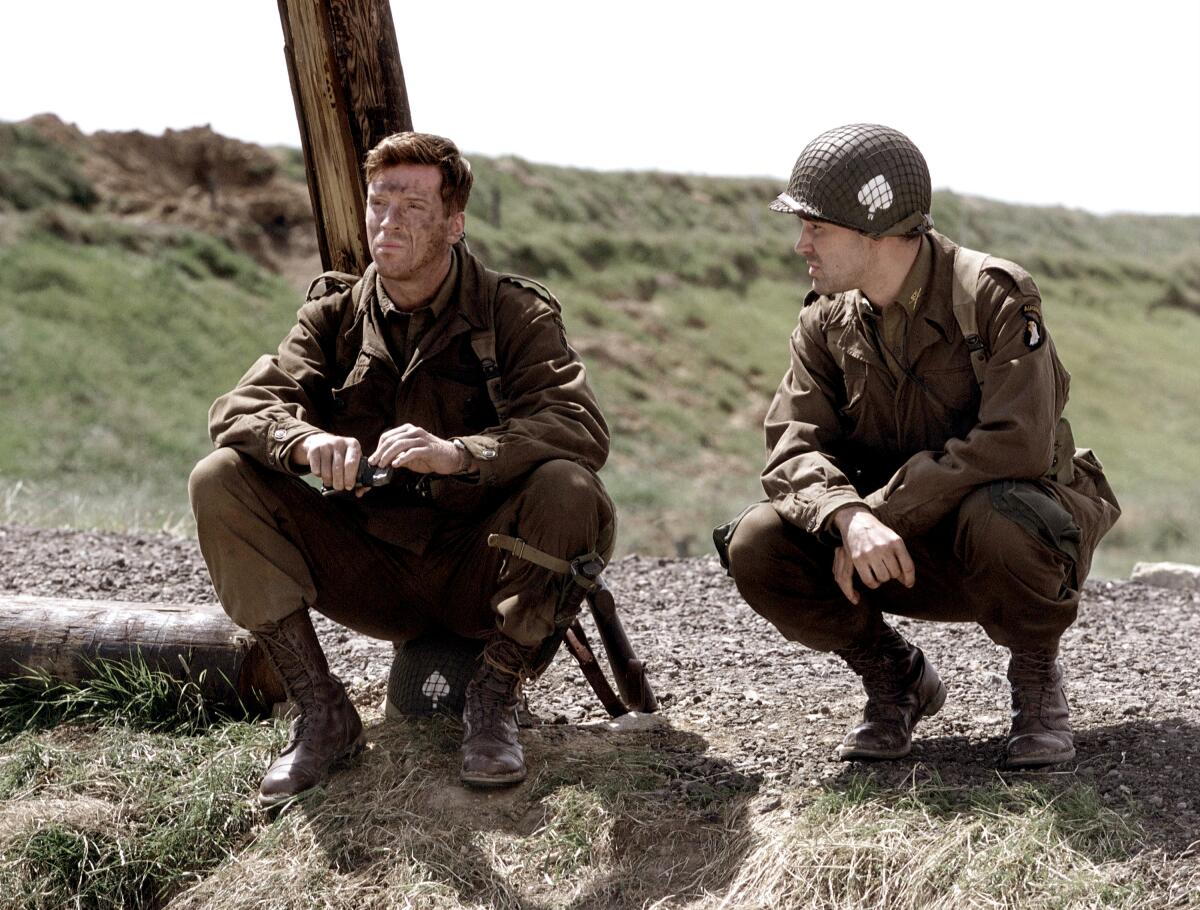Two WWII solders squat in a field.