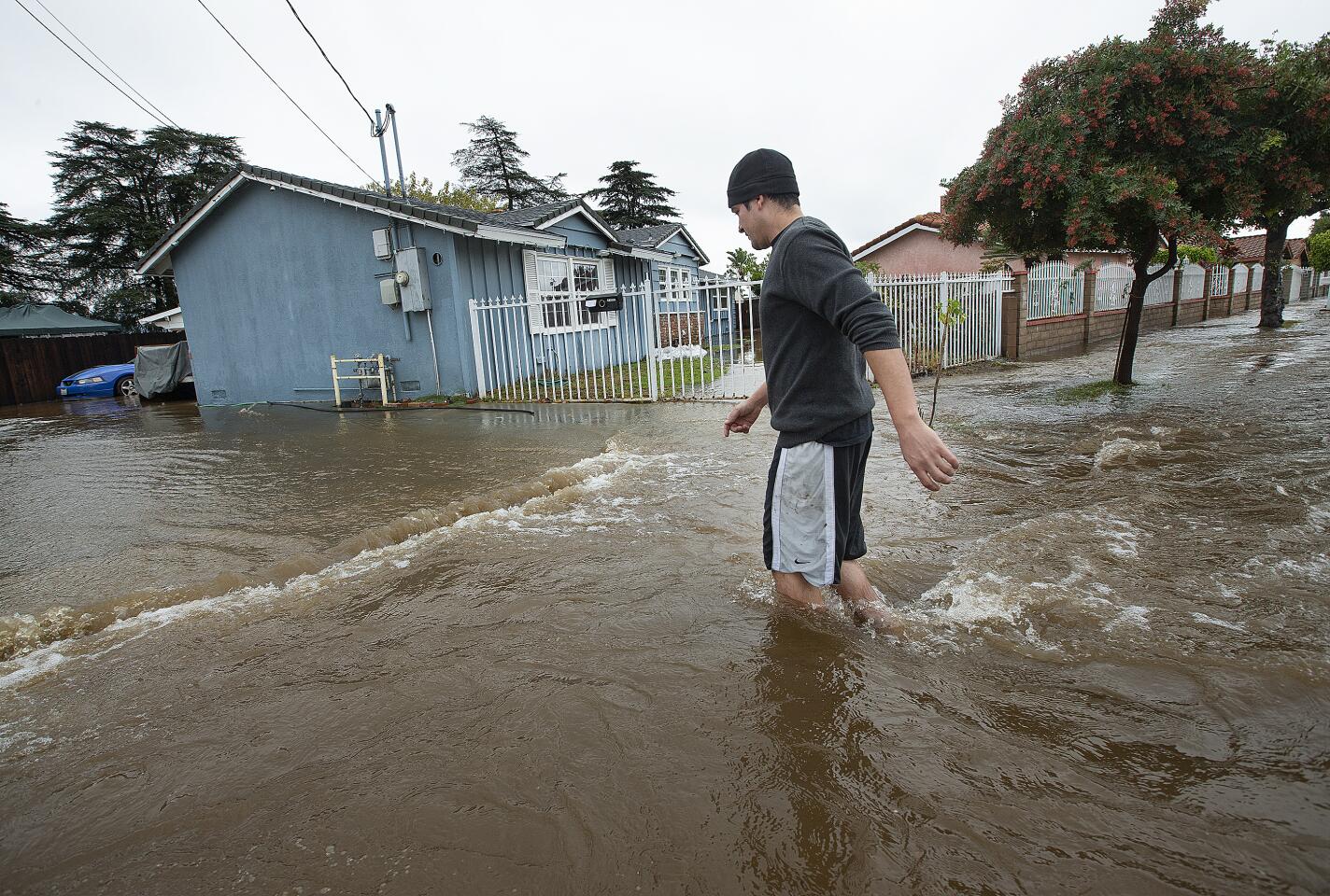 MISSION HILLS, CA-DECEMBER 4, 2019: Mission Hills resident Alberto Rodriguez, 32, walks through knee deep water on a flooded street outside of his home, at left, on Woodman Ave. The cause of the flood was a rupture from a 72 inch steel riveted trunk line that was installed back in 1914. (Mel Melcon/Los Angeles Times)