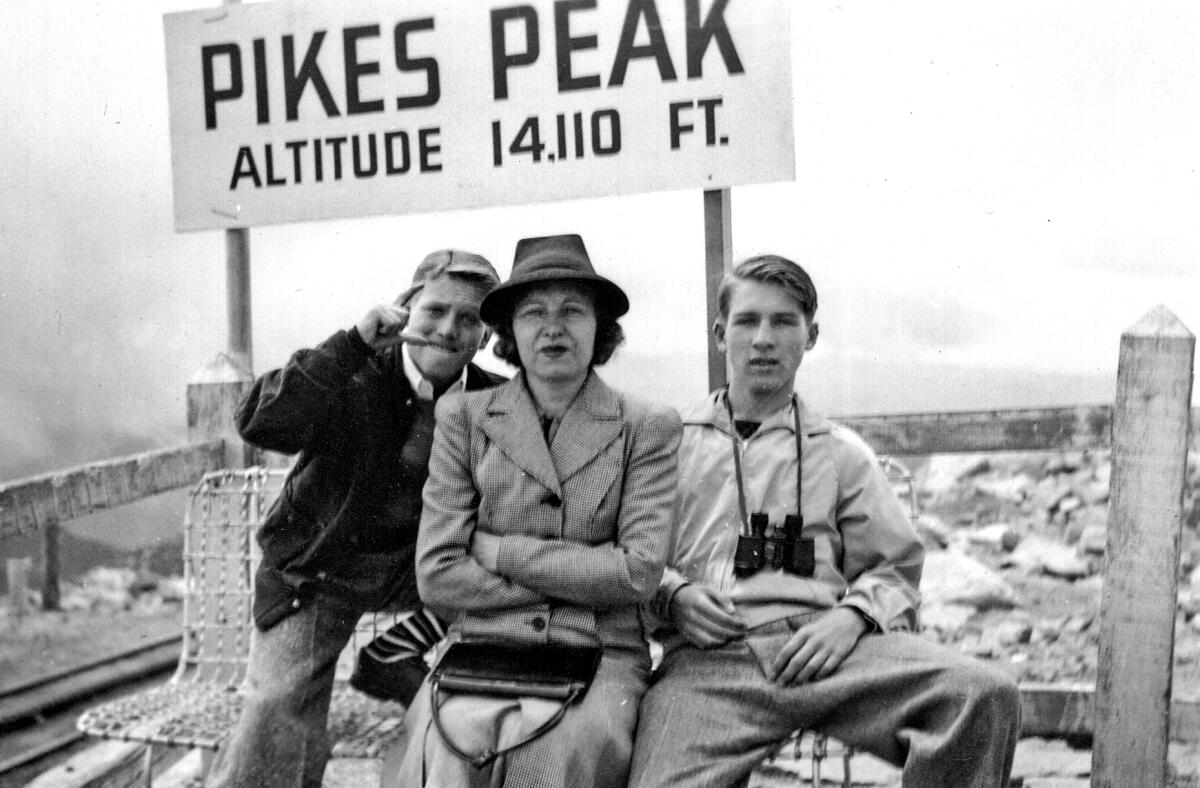 A woman and two boys sit in front of a sign that says Pikes Peak.