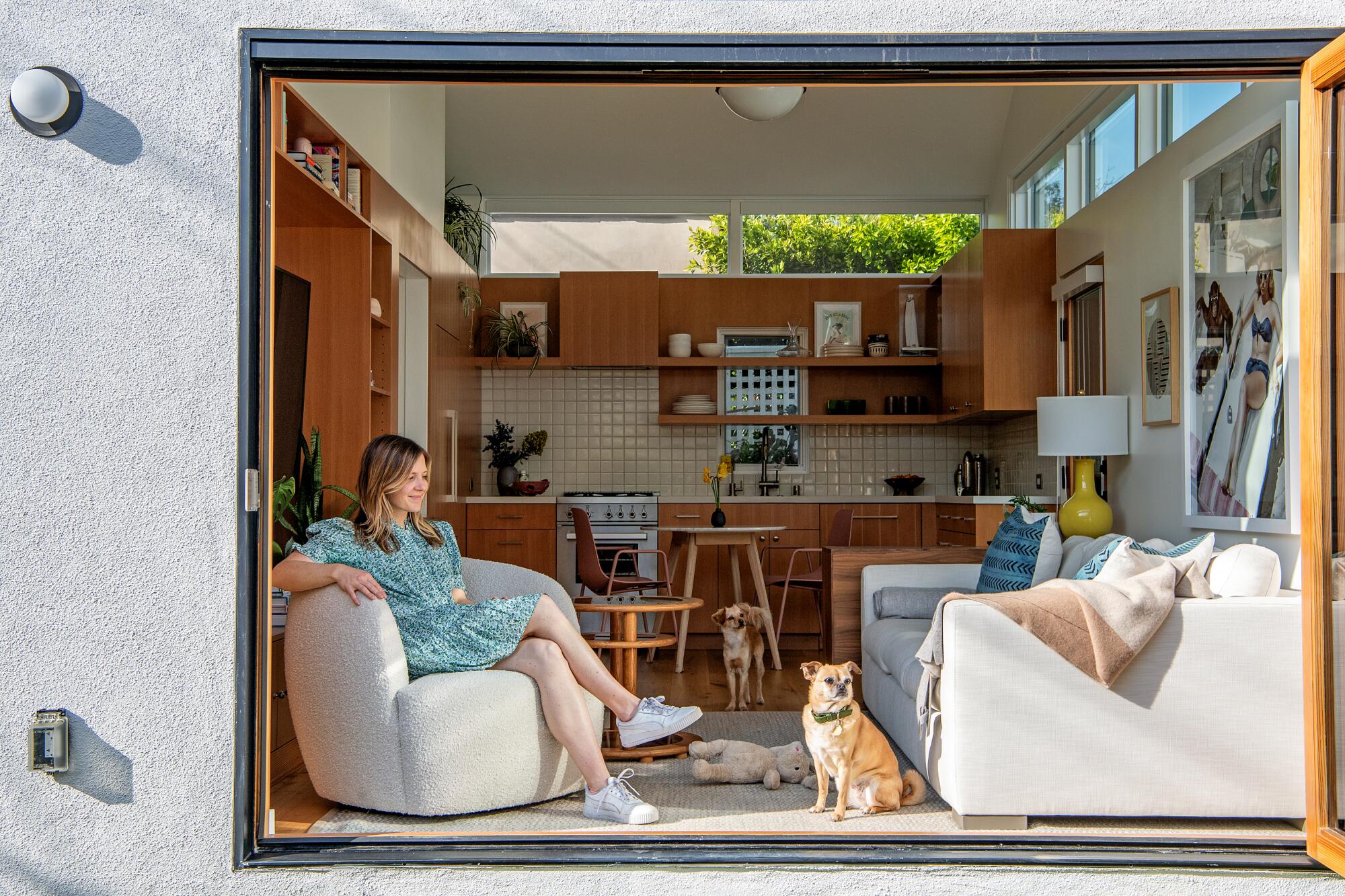 Bridget Bousa sits next to open doors in the living room of a tiny ADU, with a small dog at her feet.