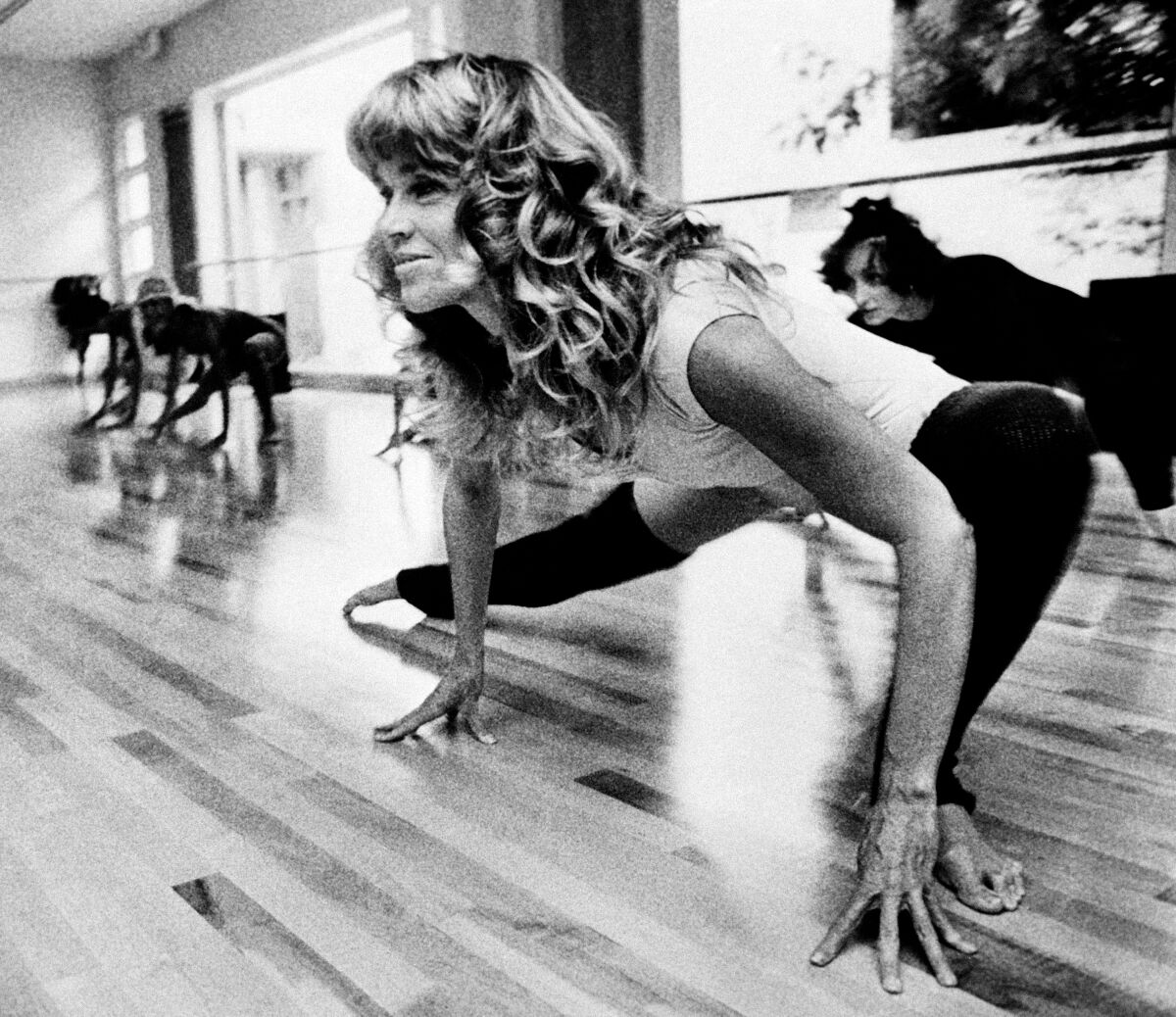 Actress Jane Fonda exercises dressed in a leotard exercises in a black and white photo
