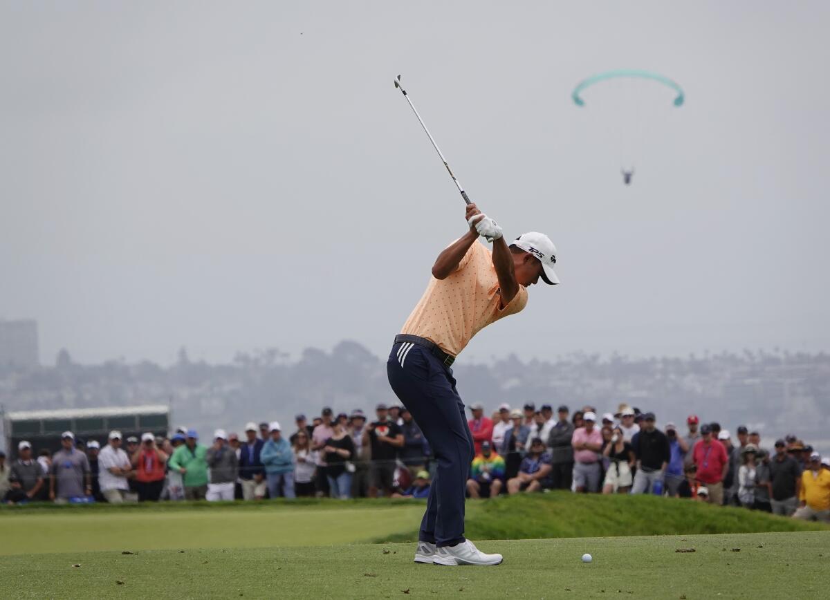 Collin Morikawa hits from the fairway on the second hole as a paraglider flies nearby.