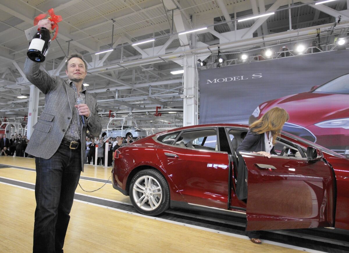 Tesla Motors Inc. CEO Elon Musk holds up a bottle of wine given as a gift from one of their first customers, right, during a rally at the Tesla factory in Fremont in July 2012.