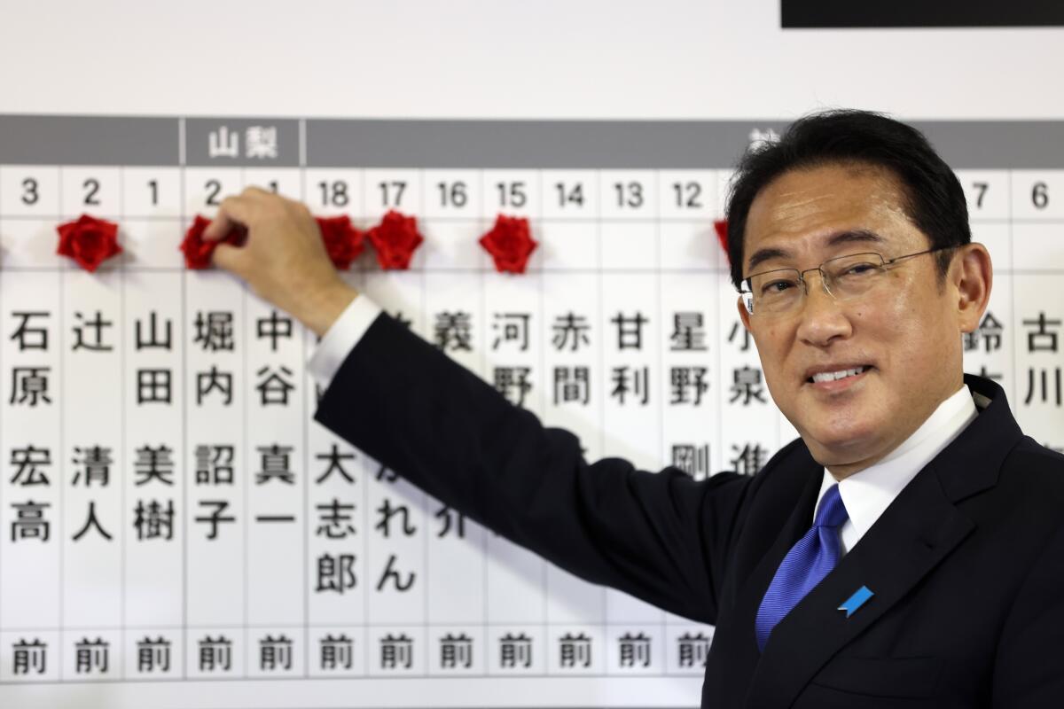 Fumio Kishida puts rosettes by successful general election candidates' names on a board