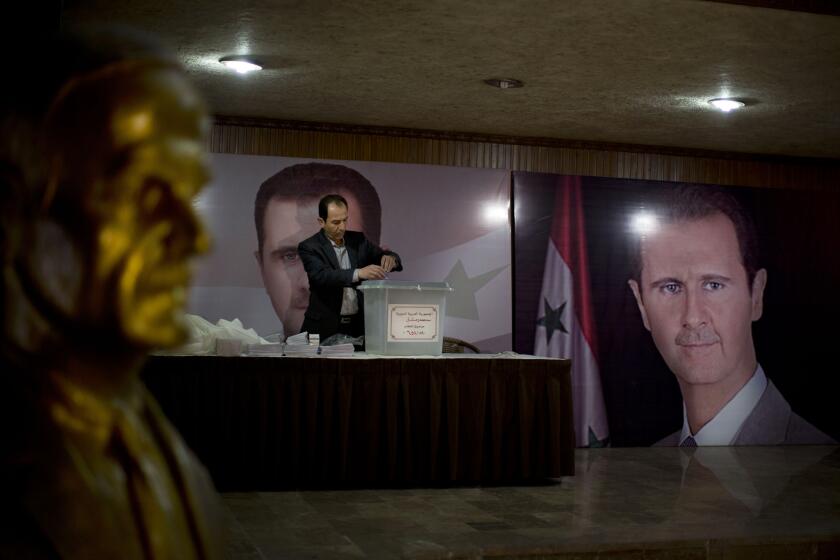 FILE - In this April 13, 2016 file photo, a Syrian election official waits for voters at a polling station with posters of President Bashar Assad during the parliamentary election in Damascus, Syria. On Sunday, April 18, 2021, Syria’s parliament speaker announced that presidential elections in the war-ravaged country will be held May 26. The election is widely expected to give Assad a fourth seven-year term. (AP Photo/Hassan Ammar, File)