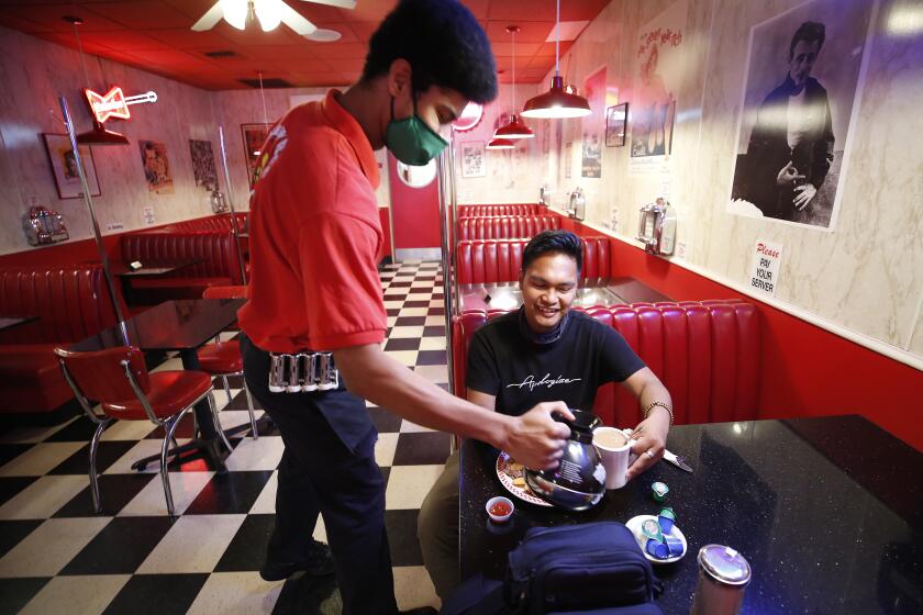 VENTURA, CA - MAY 21: Bryson Finger serves coffee to Jeric Gambon, 24, as he enjoys breakfast at Busy Bee Cafe on Main Street in downtown Ventura Thursday morning as Ventura County has become the largest county in Southern California to resume dine-in service at restaurants and in-store shopping joining a growing list of California counties that have been given permission to enter phase two of reopening after closures due to coronavirus Covid-19. Downtown on Thursday, May 21, 2020 in Ventura, CA. Downtown on Thursday, May 21, 2020 in Ventura, CA. (Al Seib / Los Angeles Times)