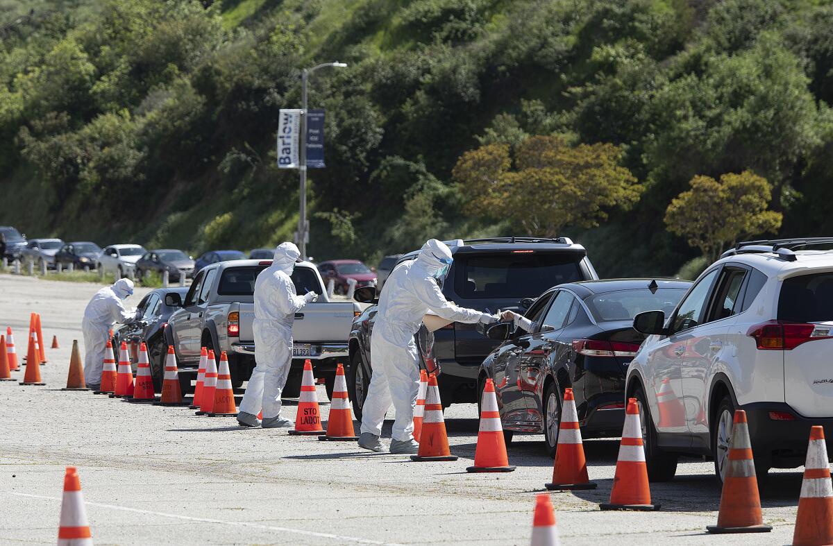 Members of the Los Angeles Fire Department wear protective gear as they hand out coronavirus test kits in a parking lot on Stadium Way, near Dodger Stadium. 