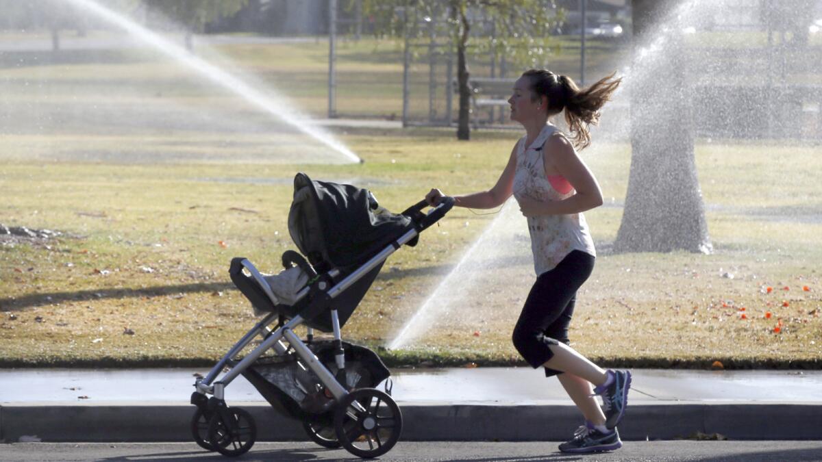 A jogger pushing a baby stroller passes sprinklers at Marina Vista Park in Long Beach.