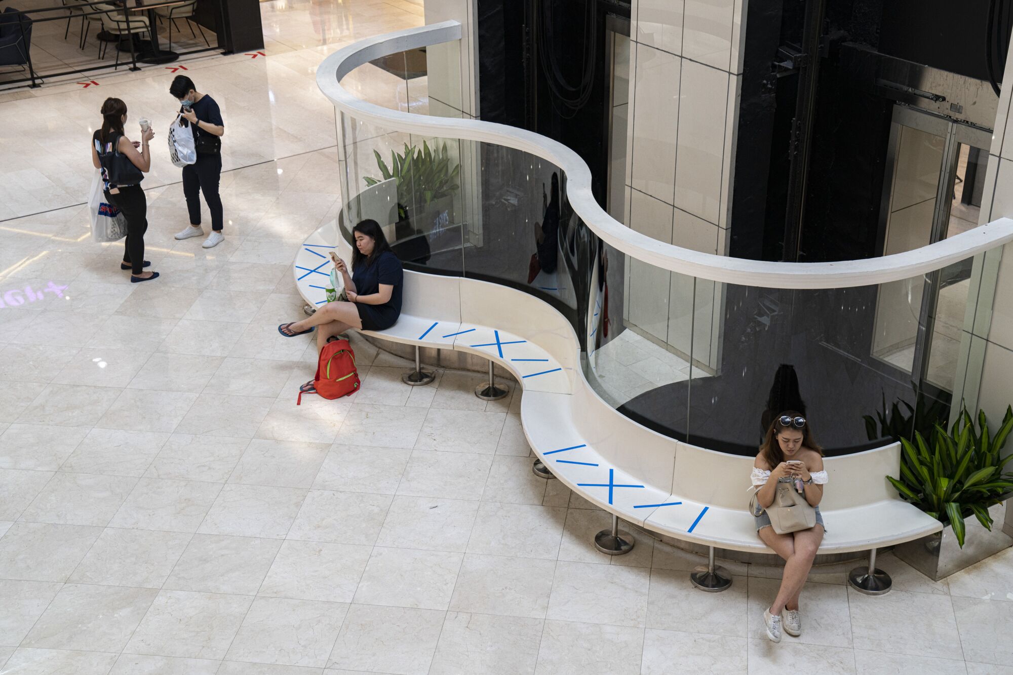 SINGAPORE: People sit along public benches at Wisma Atria shopping mall using safe-distance markers in Singapore. The government there has introduced several such measures to curb the coronavirus spread.