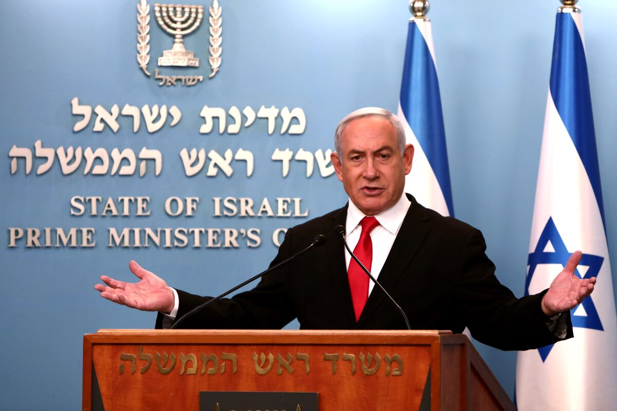 A man with arms outstretched at a podium and in front of Israeli flags