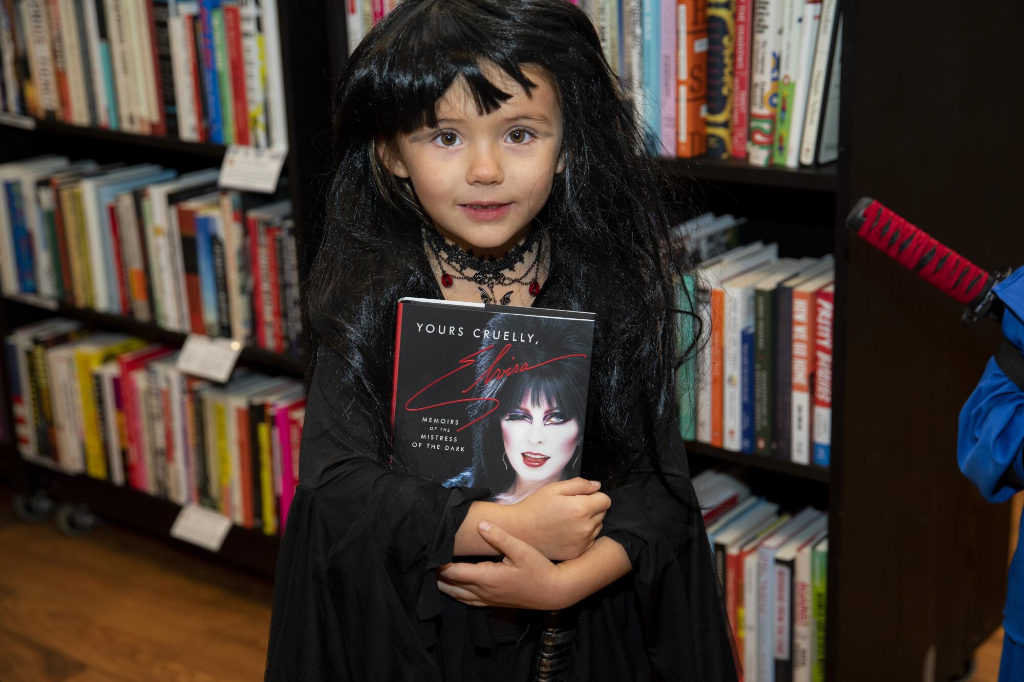 A little girl in a black wig holds a book