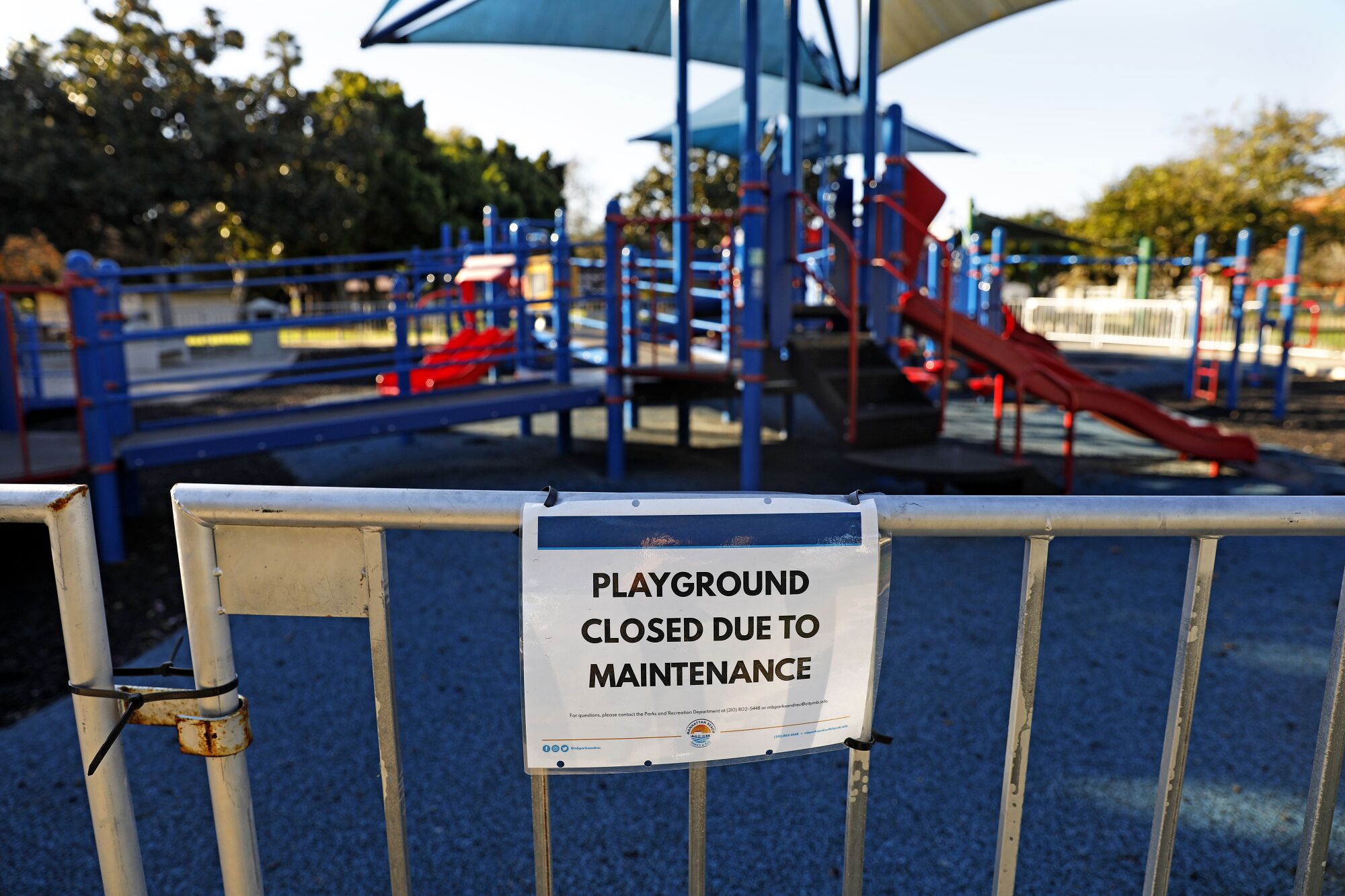 A zip tie secures the gate of a fence around a playground where a sign reads "Playground closed due to maintenance."