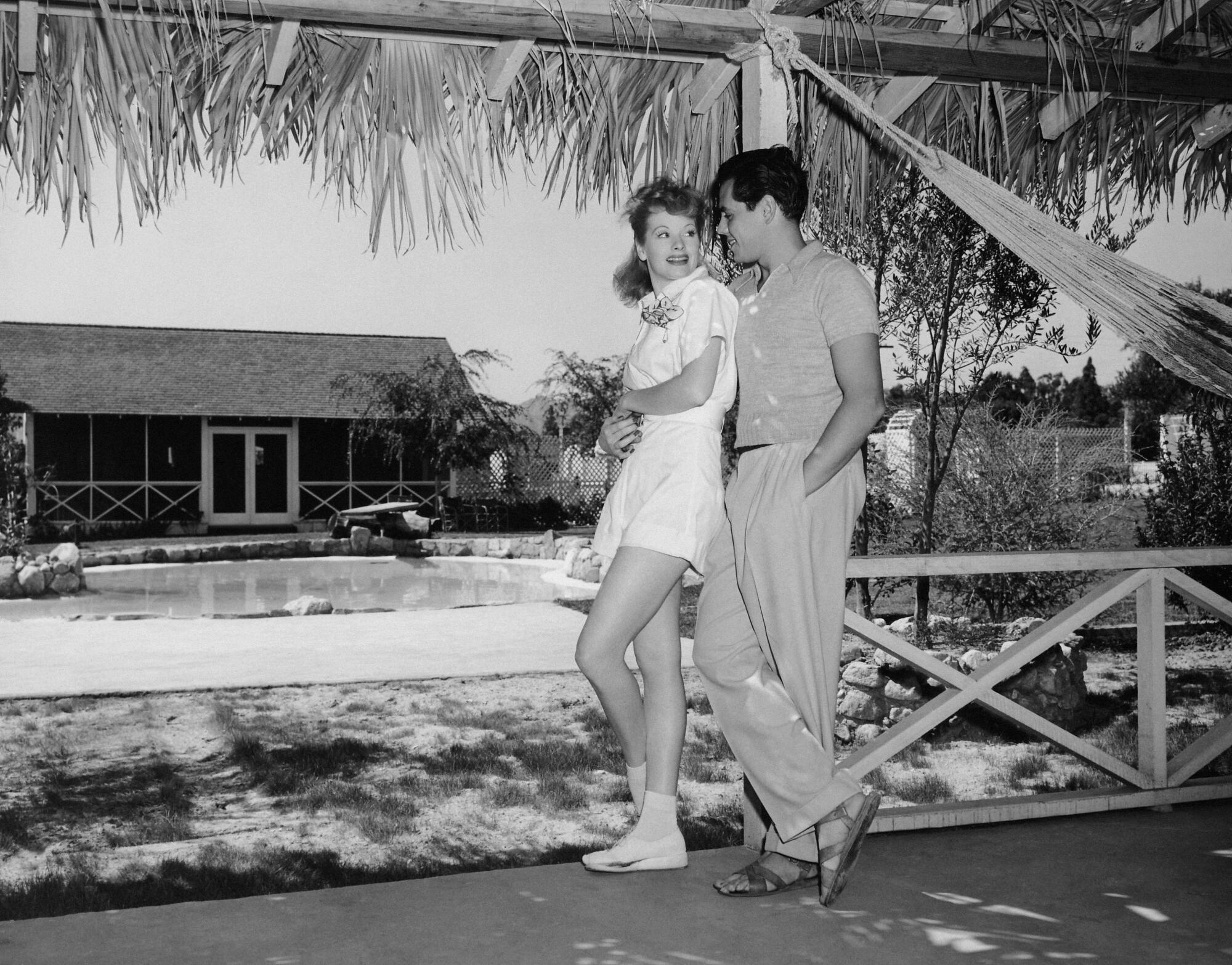 A 1942 photograph of Lucille Ball and Desi Arnaz standing together in front of their home.