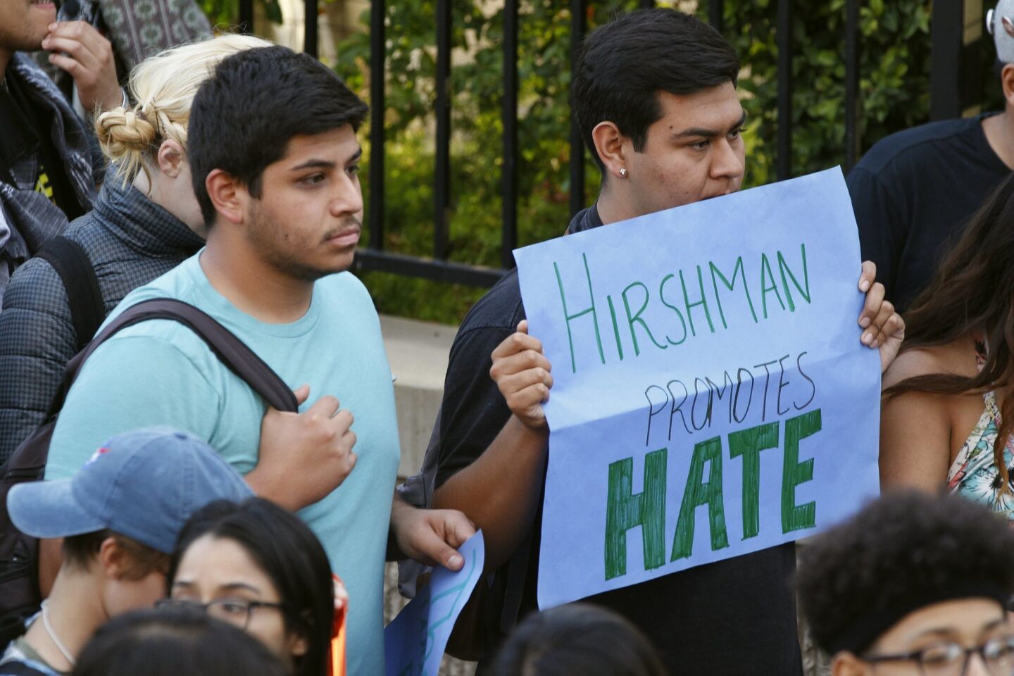 A student holds a sign against SDSU president Elliot Hirshman as others surround Hirshman.