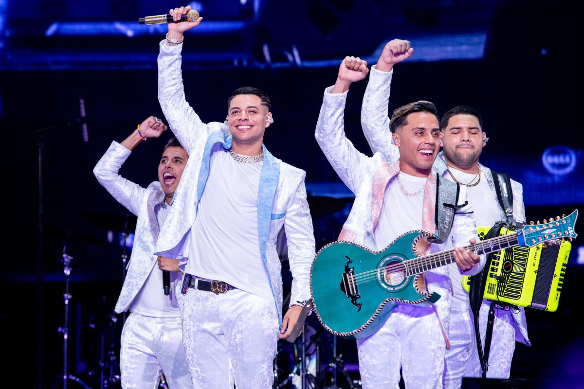 Four musicians in white suits with their arms raised, onstage