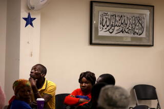 People seated in a room with a framed print in Arabic script on the wall