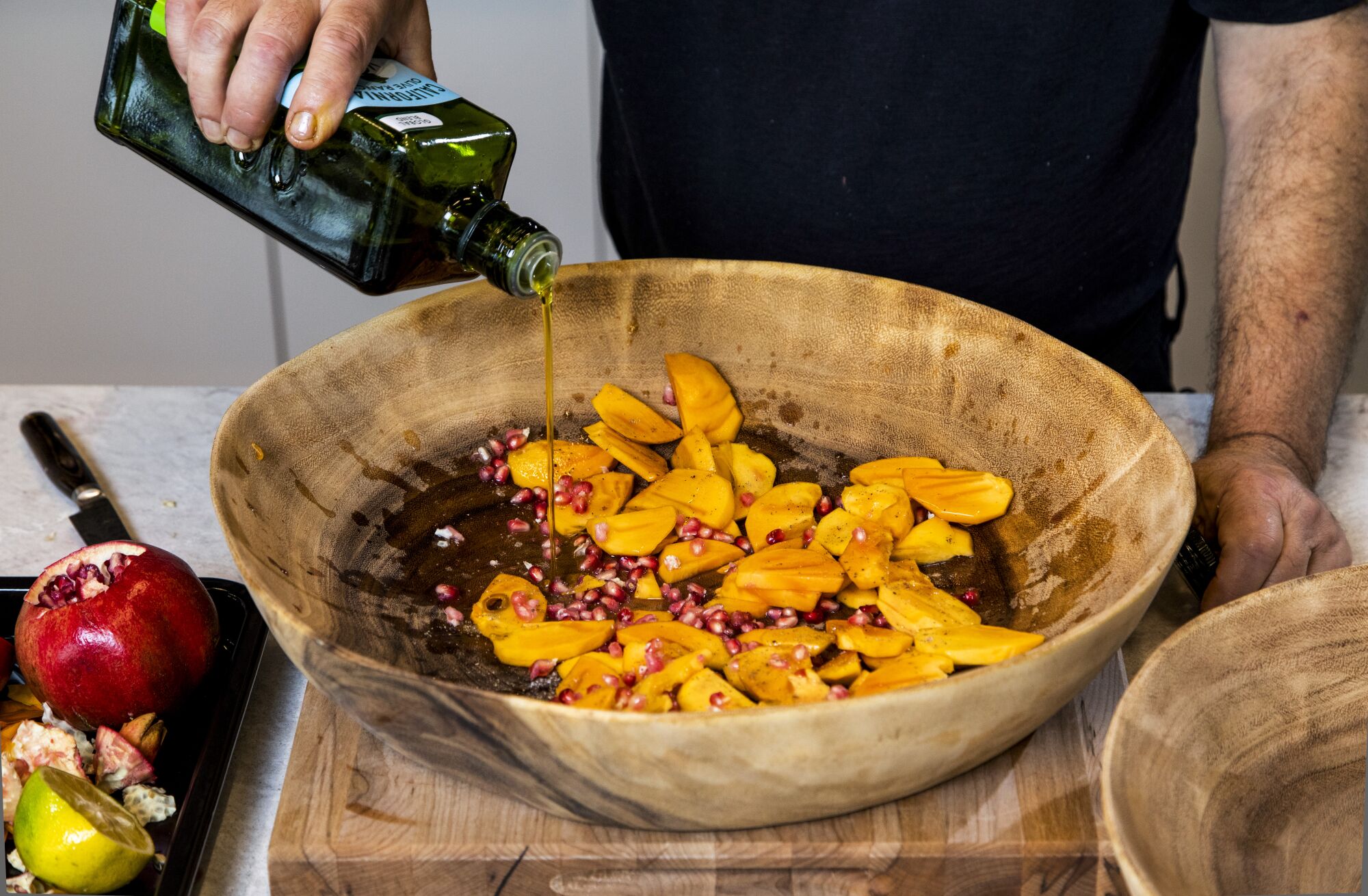 A man pours olive oil into a salad of persimmon and pomegranate seeds.