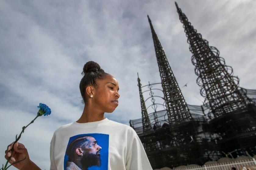 LOS ANGELES, CALIF. -- THURSDAY, APRIL 11, 2019: Ladeisha Williams, of Watts, holds a flower and wears a Nipsey Hussle shirt while paying respect and celebrating the life of Nipsey Hussle before the procession passed by the Watts Towers Art Center in Watts, South Los Angeles Thursday, April 11, 2019. (Allen J. Schaben / Los Angeles Times)