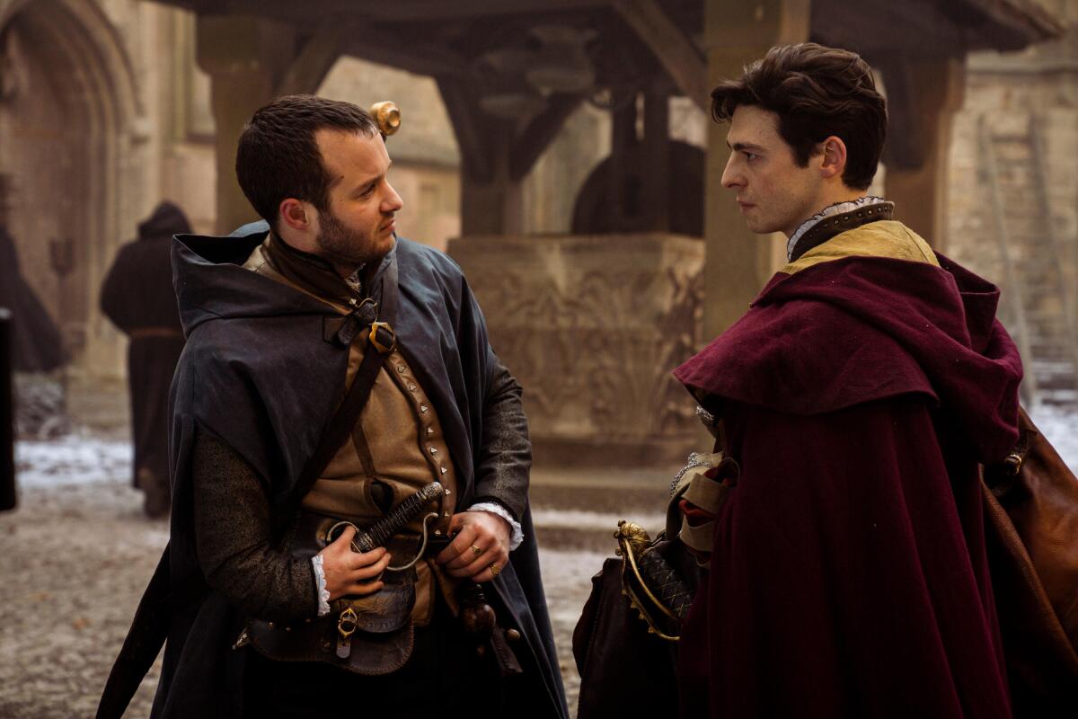 Two men in capes looking at one another.