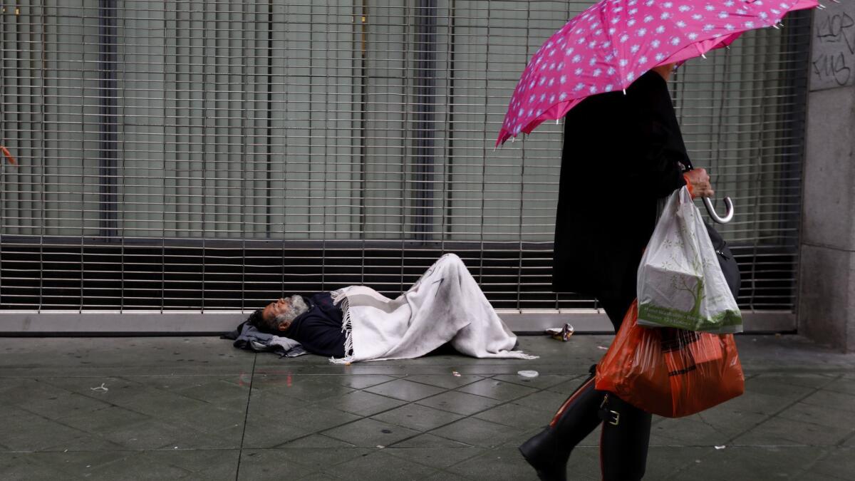 Esteban Velasquez, 54, tries to stay warm as pedestrians walk along South Broadway in downtown Los Angeles on a rainy day in January.