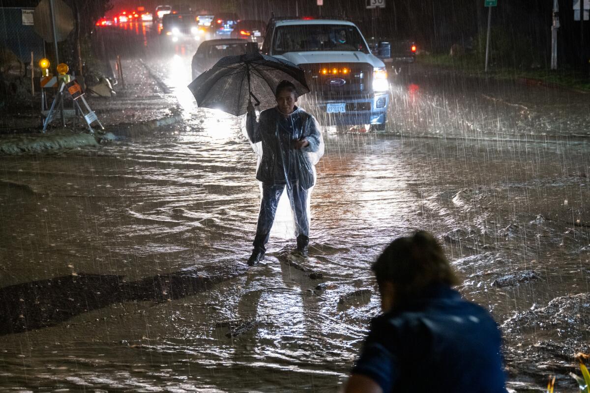 A person with an umbrella stands in a flooded street.