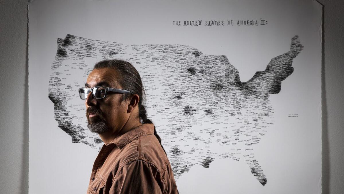 Cahuilla artist Gerald Clarke Jr. poses for a portrait with his work titled "United States of Amnesia II," at his home on the Cahuilla reservation on Monday, Nov. 26, 2018, in Anza, Calif.